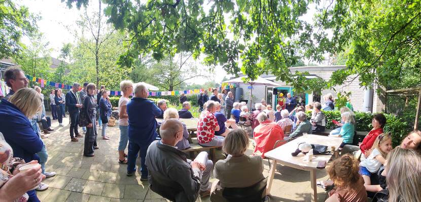 Opening van Rozet Buurtfabriek met veel mensen in de tuin zitten op stoeltjes