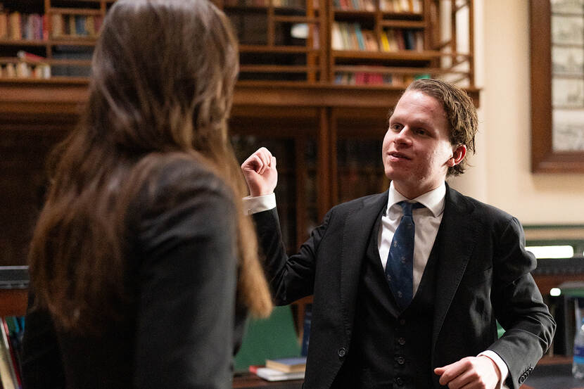 Jasmijn de Jong en Reinier Nijman staan in oude bibliotheek. Reinier zien we in het gezicht, Jasmijn op de rug. Beiden gekleed in nette kleding